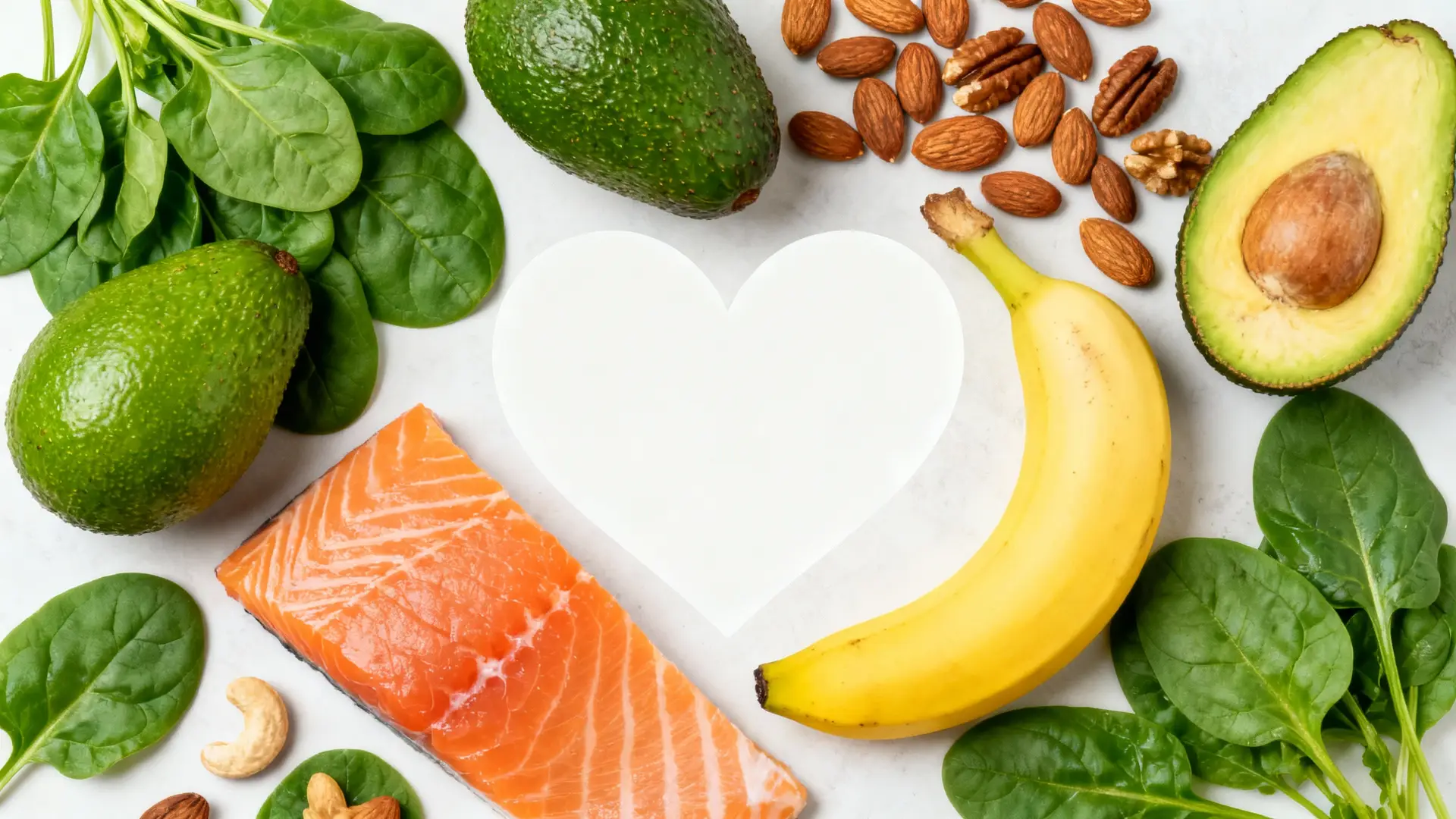 A vibrant flat lay of foods rich in magnesium and potassium, such as spinach, avocados, bananas, nuts, and salmon, arranged around a heart shape.